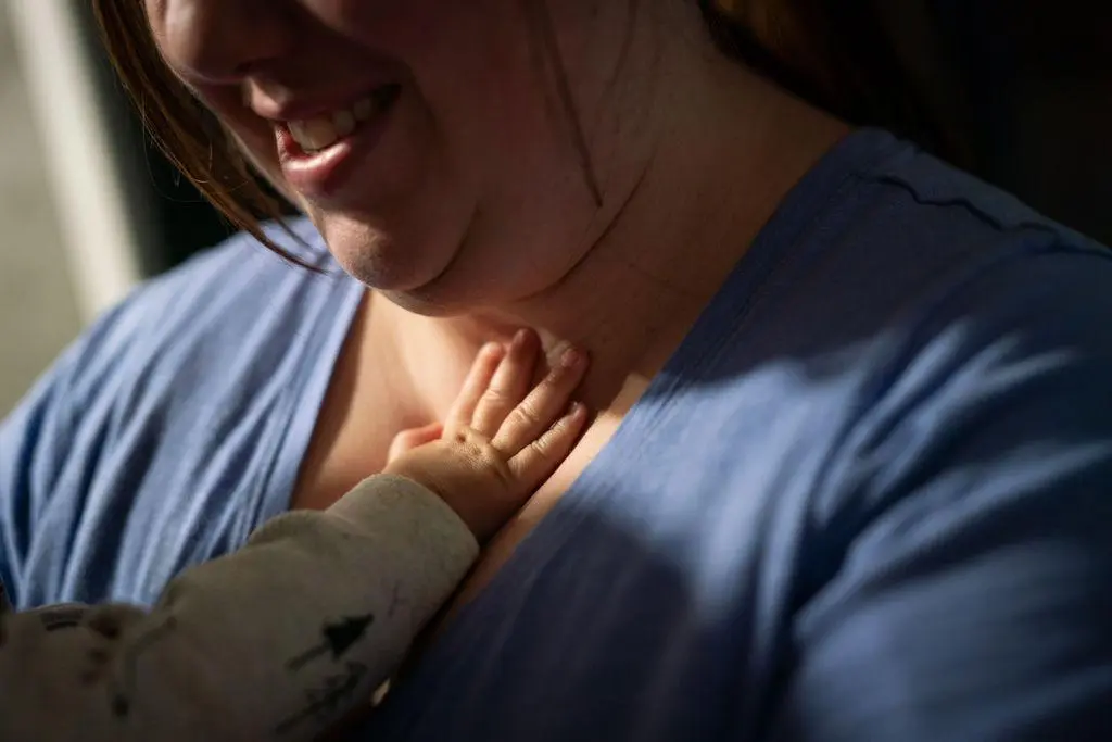 The tiny hand of an infant presses against a woman's neck. Only half of the woman's face is in view, but she is smiling down at the child.