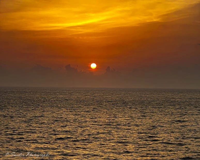 "The image shows a stunning sunset over the Caribbean Sea. The sun is low on the horizon, casting a warm, golden glow across the sky and reflecting off the calm waters below. The sky is a gradient of colors, transitioning from deep orange near the horizon to lighter shades of yellow and gold higher up. There are a few scattered clouds near the horizon, adding depth and texture to the scene. The sea appears calm with gentle ripples, reflecting the colors of the sunset. The overall atmosphere is serene and picturesque, capturing the beauty of a tropical sunset." - Copilot