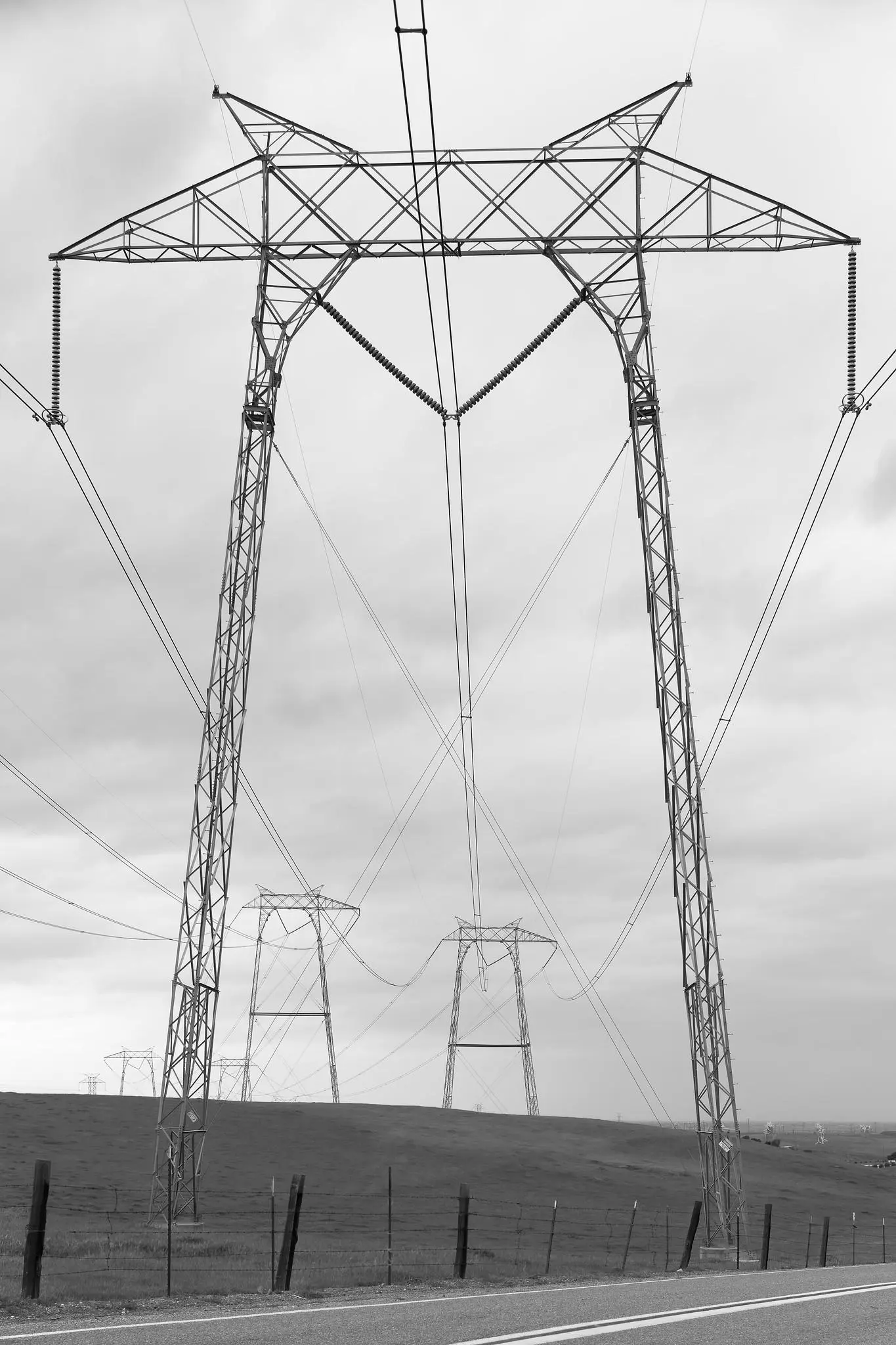 A high-voltage power transmission line pylon in a field. Other pylons are visible in the distance, connected by wires.