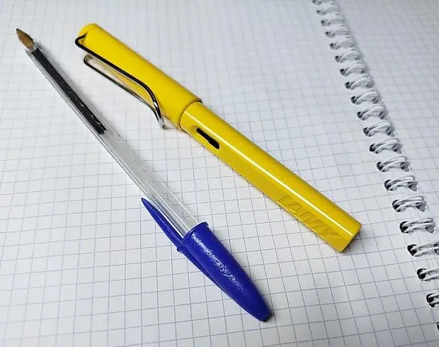 A chewed-on cristal Bic blue ballpoint pen and a (not chewed) bright yellow Lamy fountain pen, side by side