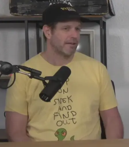 picture of Eron Jokipii aka Eron Wolf. he is wearing a Yahoo Games hat, and a yellow t-shirt with the crudely-written words "step on snek and find out" above a drawing of a green snake