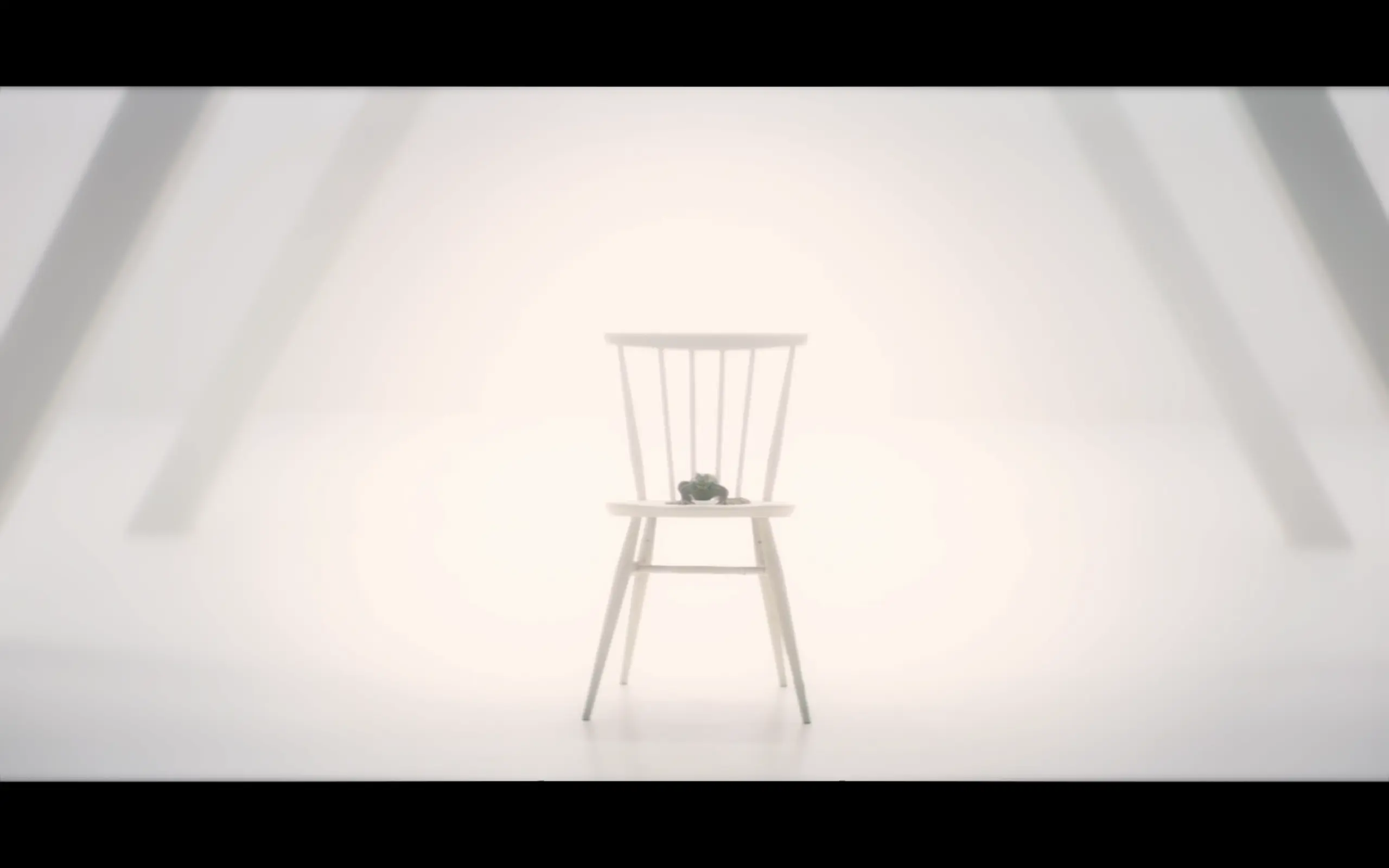 The Solitract, a powerful being taking the form of a frog, sitting on a wooden chair in a large, white room.