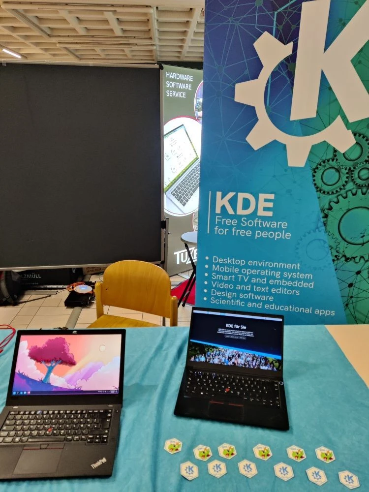 A view of KDE's booth, showing laptops running Plasma and stickers.