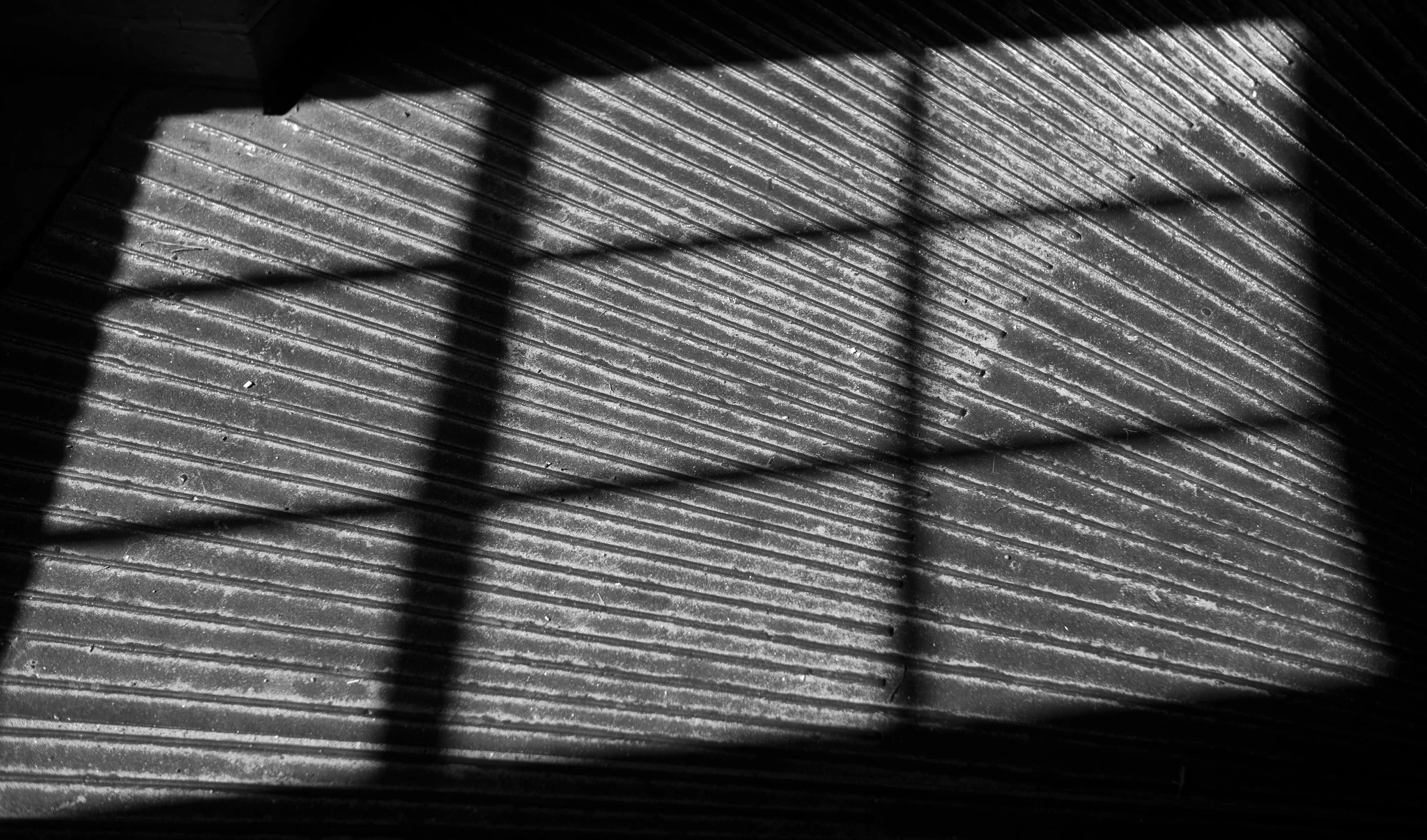 Abstract photo of the shadow cast by a window frame onto a corrugated metal floor.

