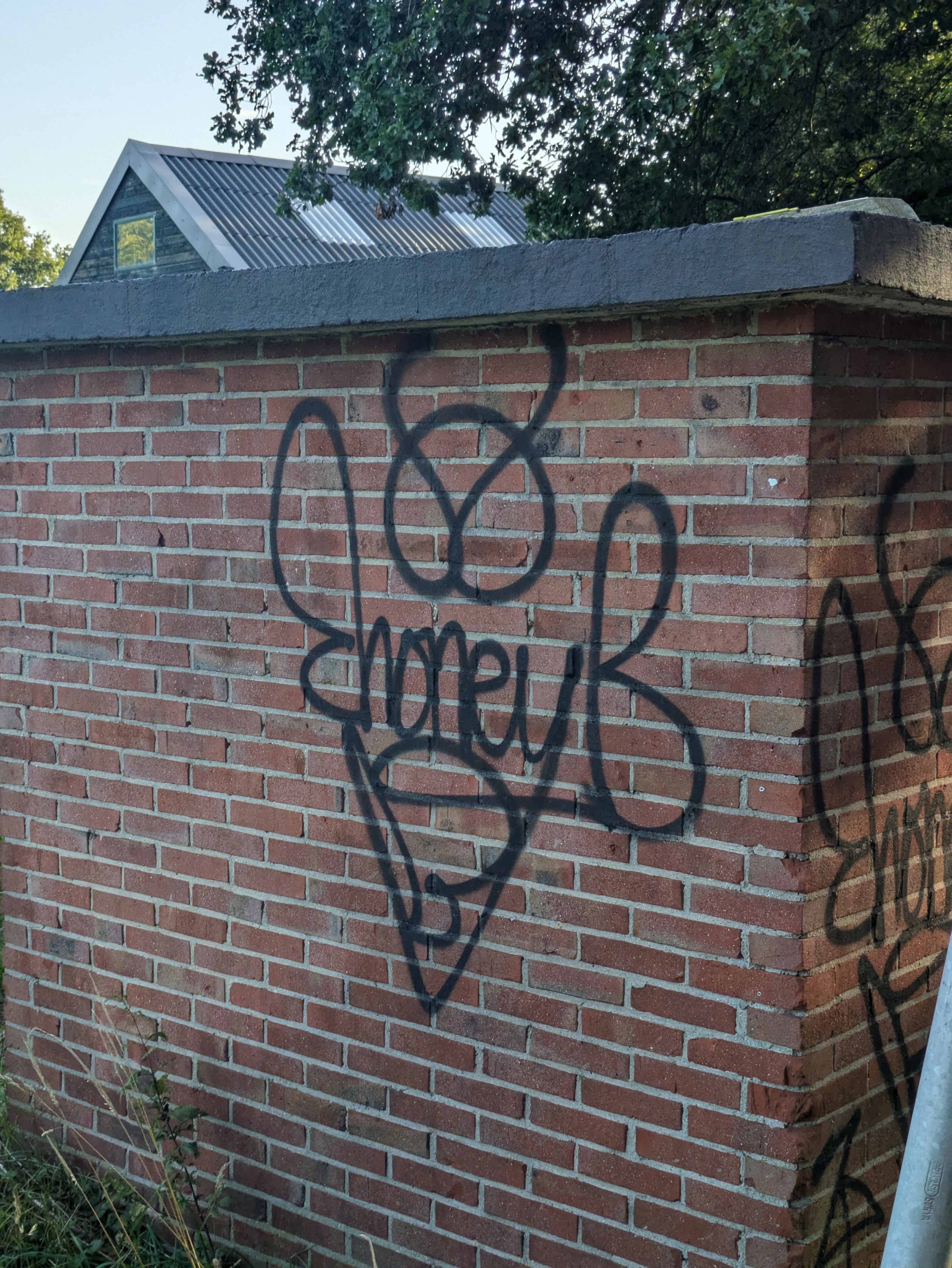 Graffiti tag "Honey B" that is stylized to look like a bee. written with black spray paint on red and broen brick wall