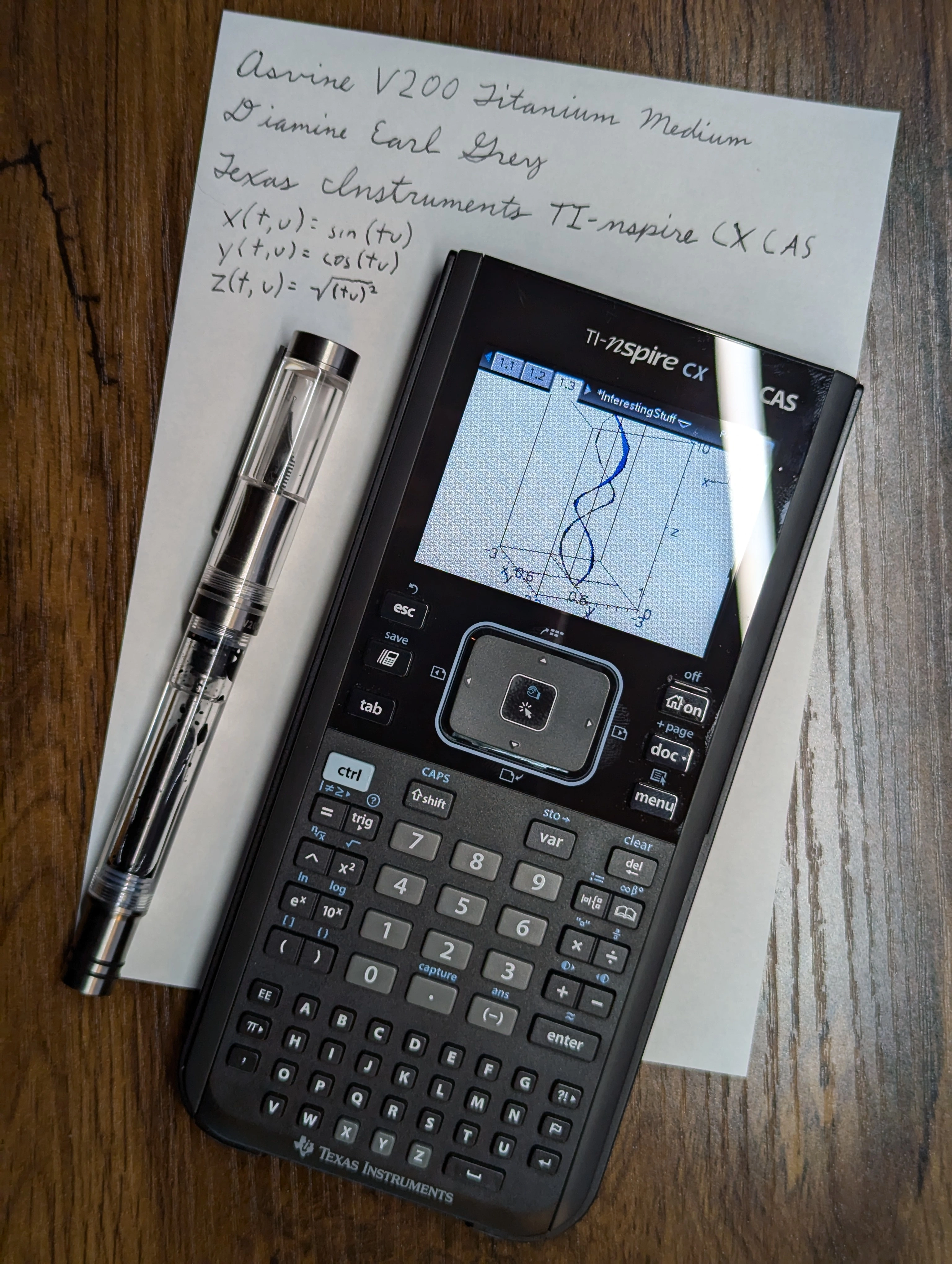 Texas Instruments TI-nspire CX CAS calculator displaying a 3-D graph.  It is next to a fountain pen and on a sheet of paper that describes the picture.