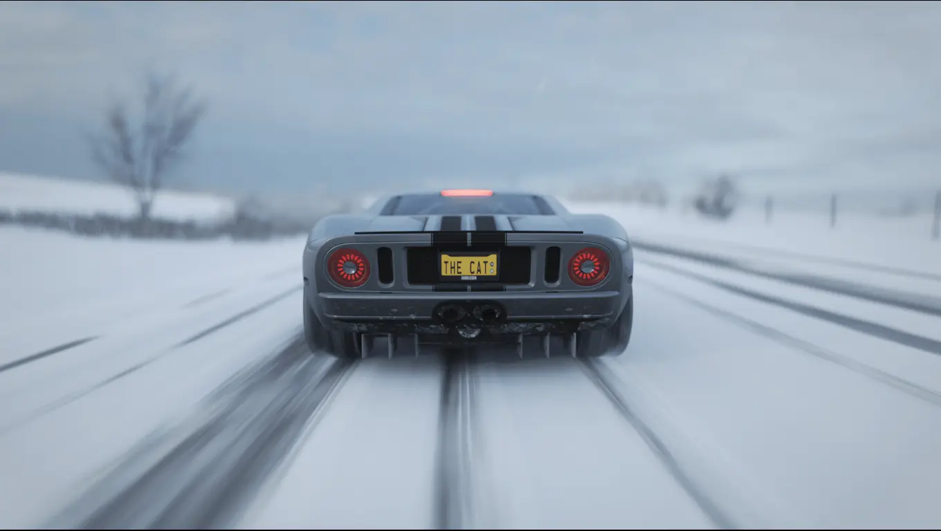 A screenshot of the back side of a grey Ford GT driving on a road partially covered with snow.