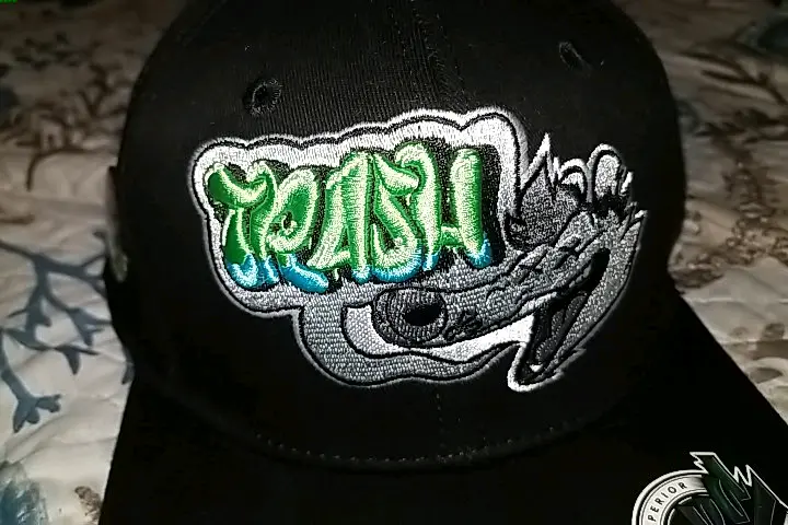 a cap with a possum's head on it and a speech bubble that says "TRASH" in big bubbly letters