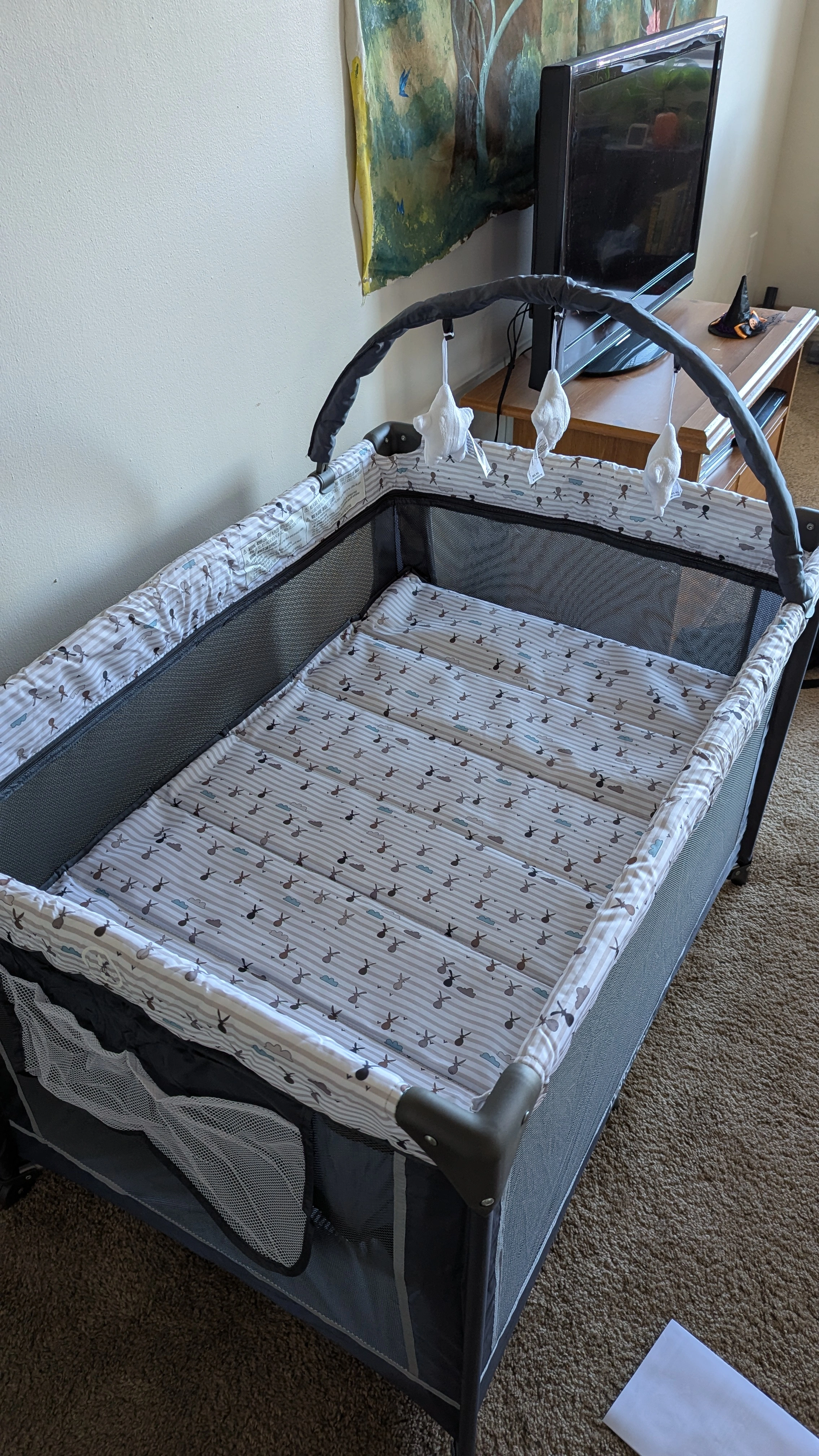 A collapsible bassinet it grey with trim elements made of fabric patterned with grey and white stripes, clouds, and stylized rabbits.