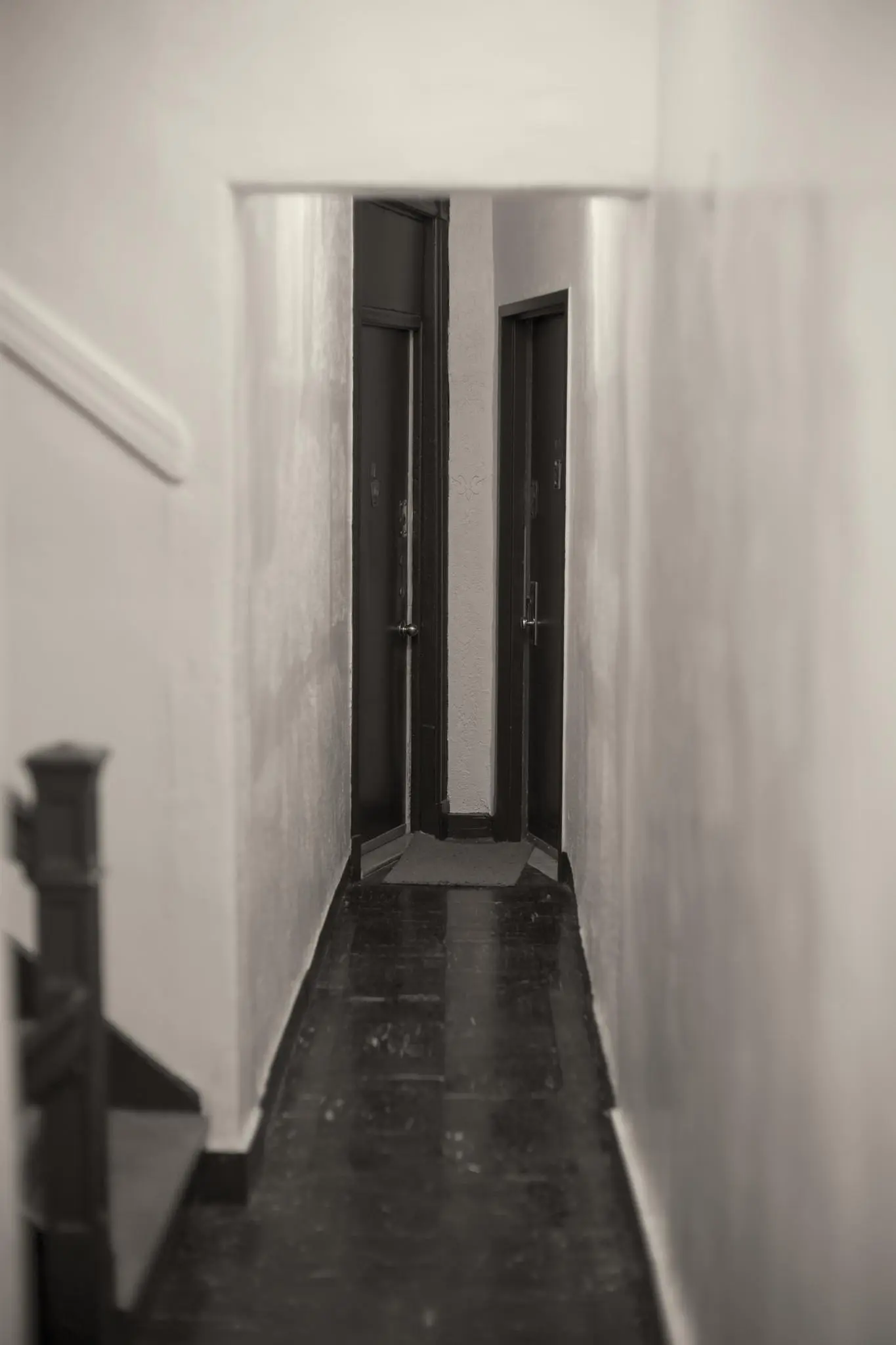 A narrow hallway in a walk-up apartment building, ending with two adjacent doors at a roughly 90 degree angle from one another.